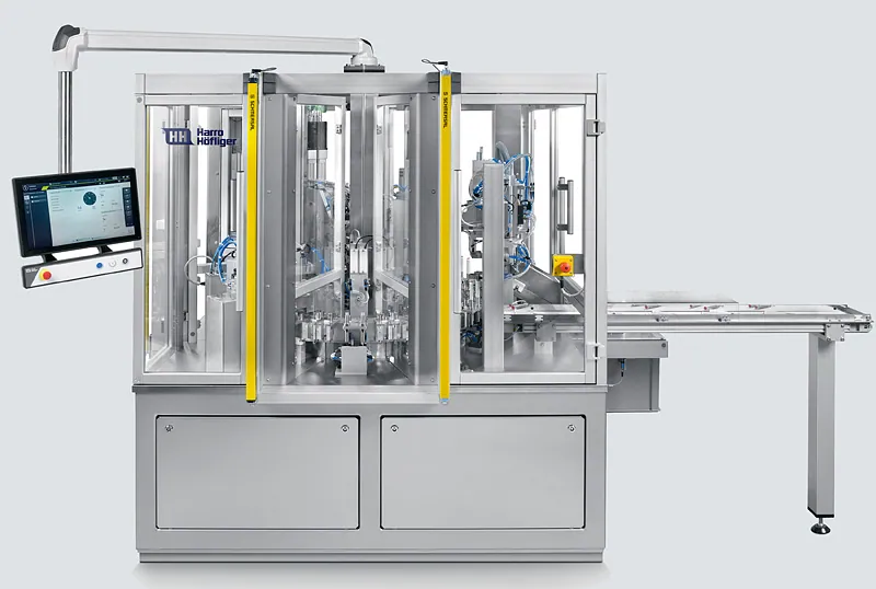 Industrial machine with transparent panels, metal frame, and control screen. Markings read "Harro Höfliger." Background is light gray.